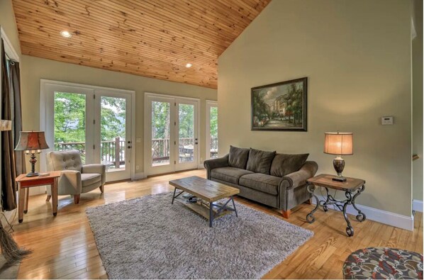 A spacious living room with a wooden ceiling, a grey sofa, a coffee table, and a painting on the wall.