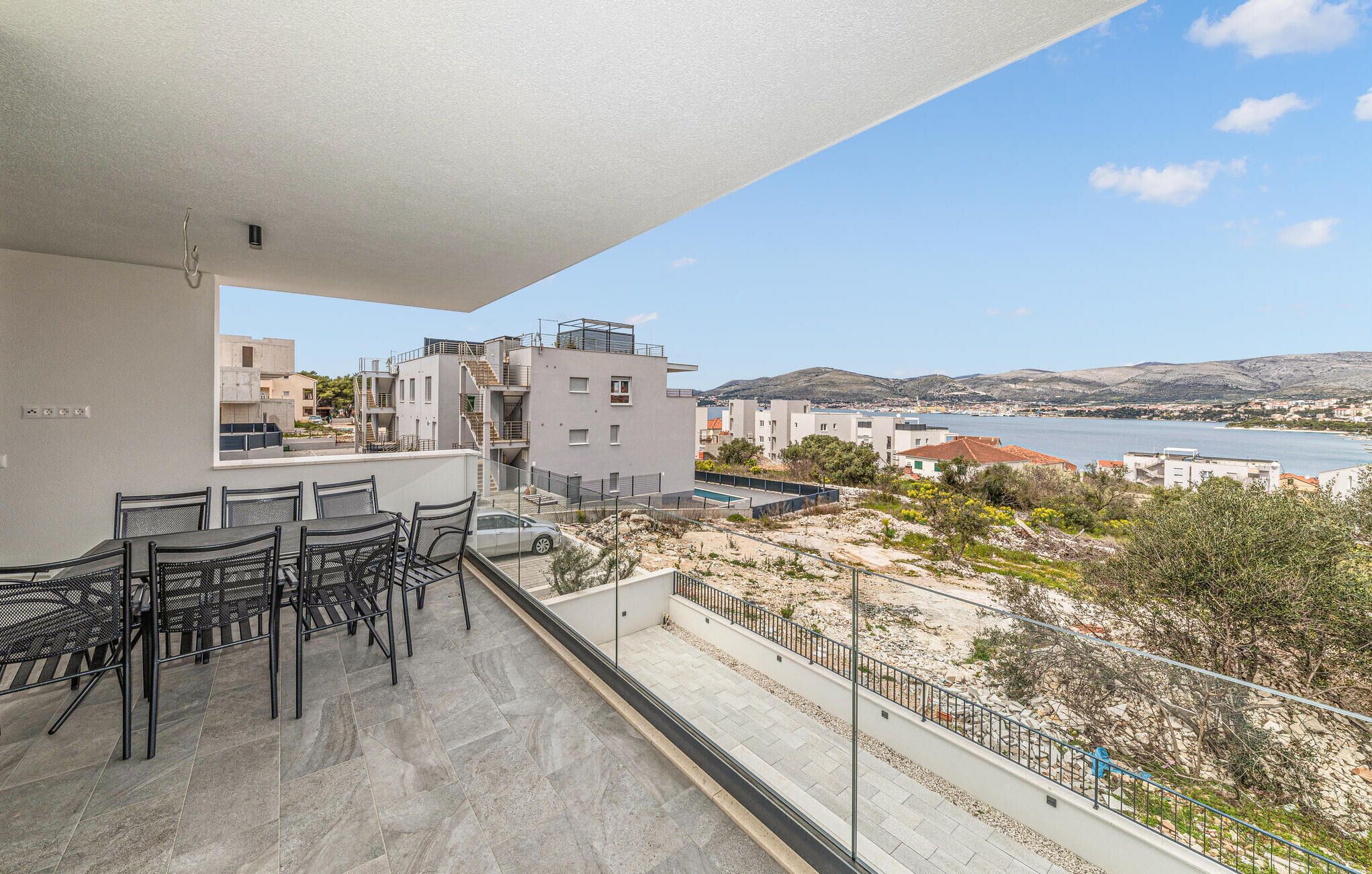 Ein Balkon mit Tisch und Stühlen mit Blick auf eine Küstenlandschaft mit Gebäuden und einem Gewässer.