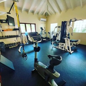 Uma academia com diversos equipamentos de exercício, incluindo esteiras e aparelhos de musculação, e um suporte com halteres.
