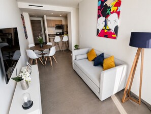 Un salon moderne comprenant un canapé, une table à manger avec des chaises, un coin cuisine et un tableau abstrait aux couleurs vives accroché au mur.