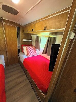 A compact RV interior with a bed, a small kitchenette, and a bathroom.