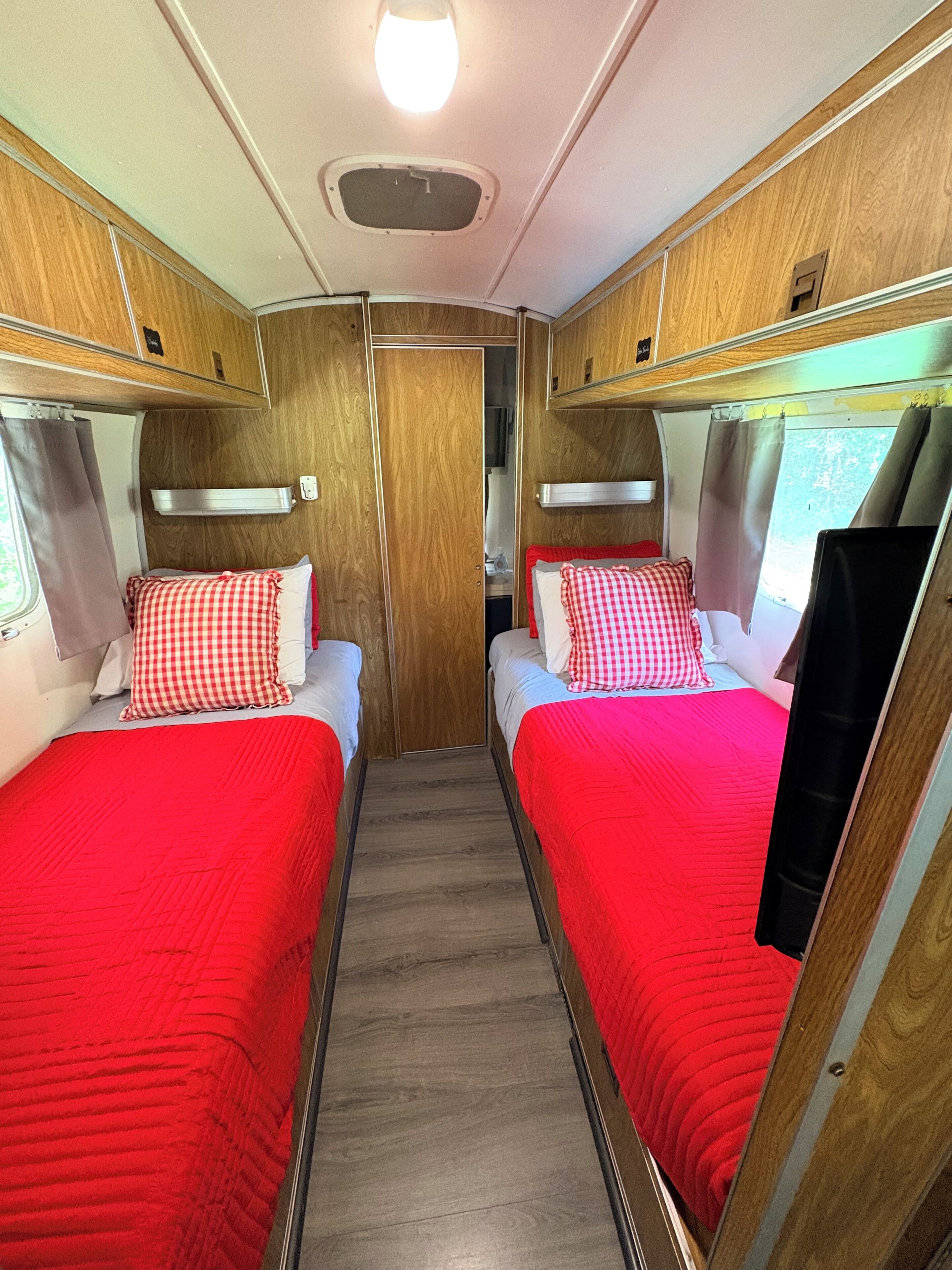 Un intérieur de camping-car compact comprenant deux lits, des panneaux de bois et une porte centrale.