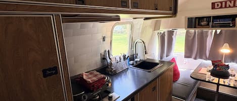 Een compacte camperkeuken met houten kastjes, een fornuis en een spoelbak.
