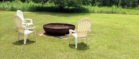 A grassy outdoor area with two Adirondack chairs and a fire pit.