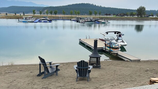 Un muelle a orillas del lago con barcos, una playa de arena y una zona verde con sillas.