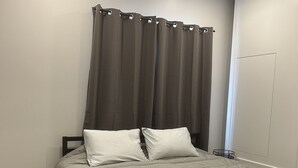 Une chambre à coucher avec un lit, des rideaux gris, une armoire blanche et un plancher en bois.