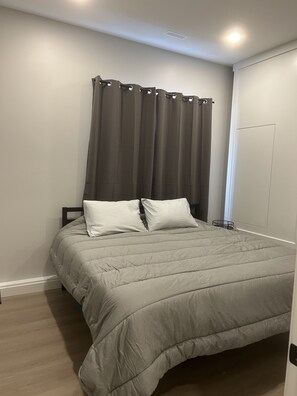 Une chambre à coucher avec un lit, des rideaux gris, une armoire blanche et un plancher en bois.