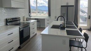Una cocina moderna con armarios blancos, una isla central y un ventanal con vistas a montañas.