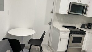 Une cuisine compacte avec des meubles blancs, un four à micro-ondes, une cuisinière et une petite table à manger avec deux chaises.