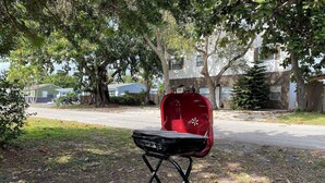 Un barbecue portable installé dans un espace verdoyant, avec des arbres et un bâtiment en arrière-plan.