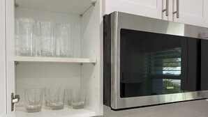 Une cuisine équipée d’un four à micro-ondes encastré et d’une étagère où sont rangés des verres transparents.