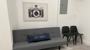 Un canapé gris avec un coussin sur lequel est écrit « NE VOUS APPROCHEZ PAS » et deux chaises noires.