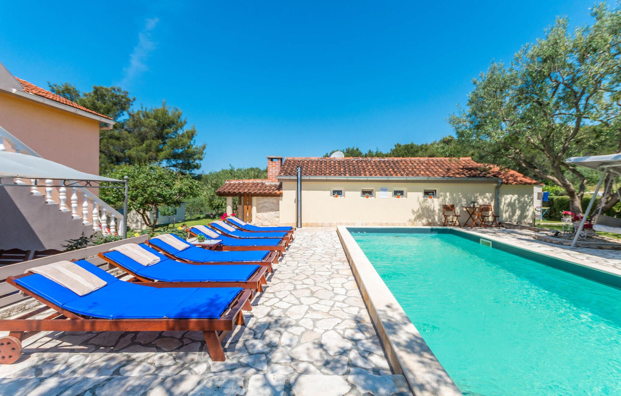 Un área de piscina con sillas reclinables azules y un deck de baldosas de piedra.