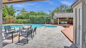 Un jardin avec une piscine, des meubles de patio et un espace de détente extérieur doté d’un toit de chaume.