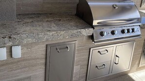 A stainless steel barbecue grill with a chimney, integrated into a kitchen counter with a stone backsplash. - Luxury Living in the Heart of NY (Yonkers)