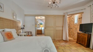 A bedroom with a bed, a TV, a wardrobe, and a bathroom visible through an open door. - SERENITY Villa for 8 By Sunset (Grasse)
