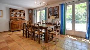 A dining area with a wooden table and chairs, a cabinet with dishes, and a view through glass doors. - SERENITY Villa for 8 By Sunset (Grasse)
