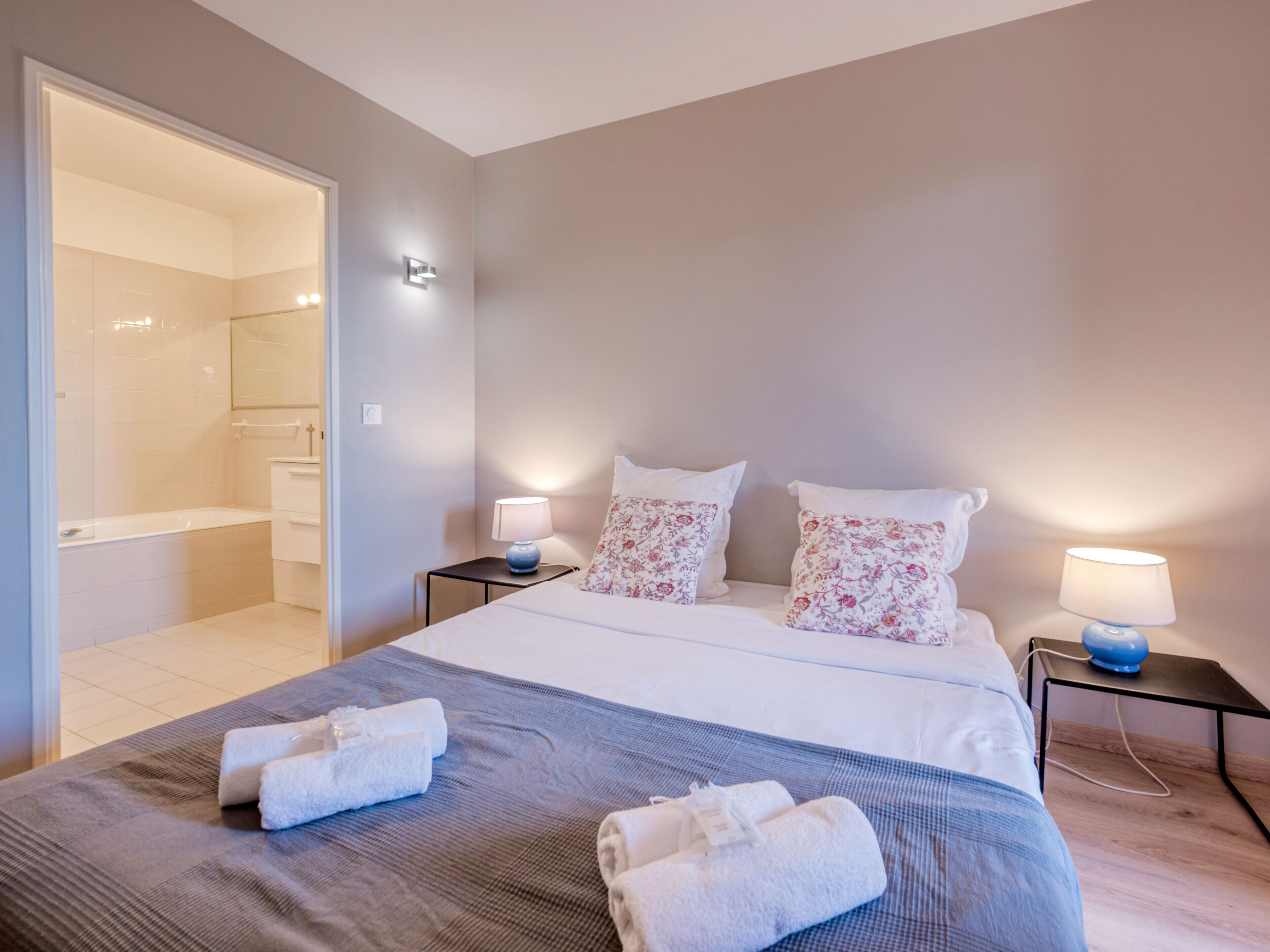 A hotel room with a bed, two bedside tables with lamps, a bathroom visible through an open door, and towels on the bed.
