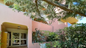 A building with a pink exterior, a tiled entrance, and a garden with various plants. - LA BADINE Appartement AirCo Pool for 4 By Sunset (Antibes)