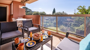 A balcony with wicker furniture, a table set with plates, cups, and a basket of bread. - LA BADINE Appartement AirCo Pool for 4 By Sunset (Antibes)