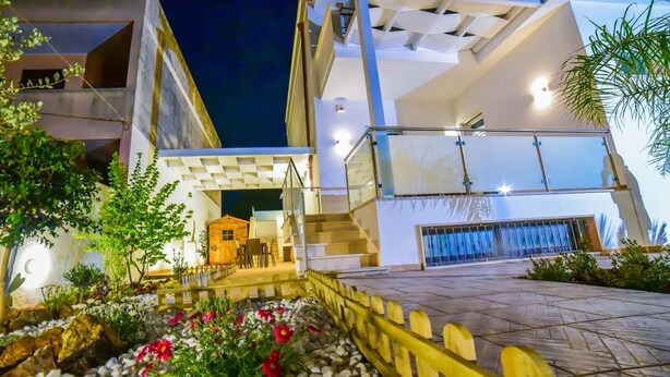 Un edificio moderno con una escalera que conduce a un nivel superior, una pequeña estructura de madera y un jardín con rocas y flores.