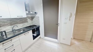 Cocina moderna con estufa a gas, pileta y horno, alacenas blancas y una puerta de madera.