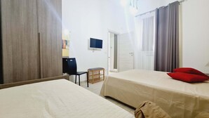 Habitación de hotel con dos camas, un escritorio, una silla, un televisor y una puerta que da a un balcón.