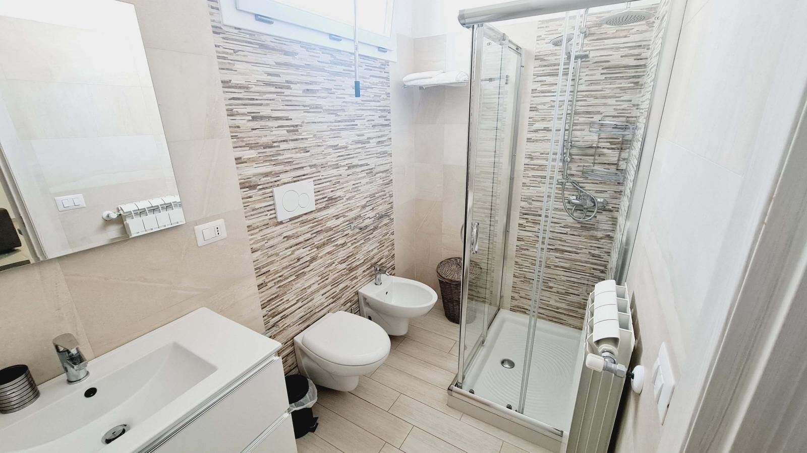 A modern bathroom with a glass-enclosed shower, a white sink, and two toilets.