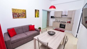 A compact living space with a sofa, dining table, chairs, a kitchen area, and artwork on the walls.