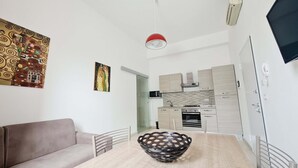 A modern living room with a sofa, a dining table with a decorative bowl, a kitchen with light wood cabinets, and a red pendant light.