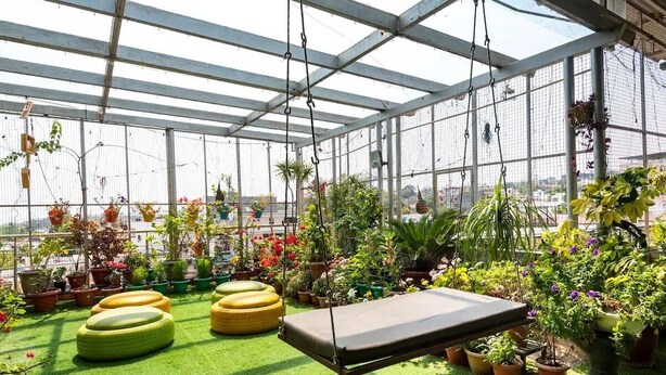 A greenhouse with hanging planters, a swing, and a variety of potted plants.