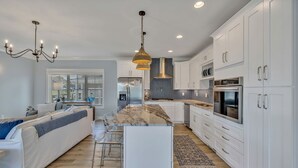 A modern kitchen with white cabinetry, a marble island, stainless steel appliances, and a chandelier. - Bright airy lakeside home in gated community (Winchester)