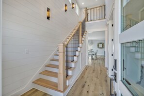 Una escalera con escalones de madera y barandillas negras que conduce a un segundo piso con balcón.