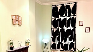 Een woonkamer met een open haard, een zwart-wit abstract gordijn, een glazen salontafel, een gele fauteuil en een zwarte leren bank met rode kussens.