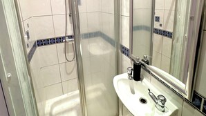 Een badkamer met een glazen douchecabine, een wastafel met spiegel en betegelde wanden.