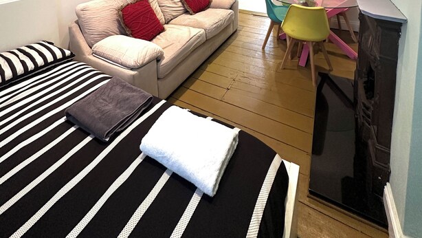 Een knus woongedeelte met een bank, een eettafel met stoelen, een bed met gestreept beddengoed en een open haard.