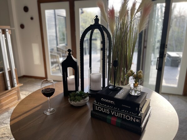Una mesa redonda de madera con una copa de vino, una vela, un farol decorativo y una pila de libros de una marca de lujo.