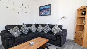 Una sala de estar con un sofá modular, una mesa de centro de madera, un tapiz estampado, un globo montado en la pared y una fotografía enmarco de un paisaje urbano.