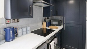 Cocina moderna con armarios oscuros, una placa de inducción negra, microondas y hervidor. Hay recipientes etiquetados para té, azúcar y café.