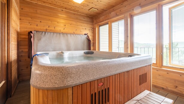 Eine Holzhütte mit Whirlpool, großen Fenstern und einer Holzbalkendecke.