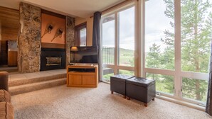 Ein Wohnzimmer mit Steinwand, Kamin, Fernseher und einem großen Fenster mit Blick auf Bäume.