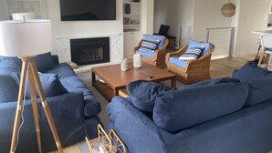 A living room with a fireplace, blue sofas, wicker chairs, a coffee table, and a TV mounted on the wall. - Long Beach Cottage with Lake views and one block walk to Stop 26.   (Long Beach)