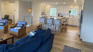 A modern living room with a blue sofa, wicker chairs, and a dining area with white cabinets and bar stools. - Long Beach Cottage with Lake views and one block walk to Stop 26.   (Long Beach)