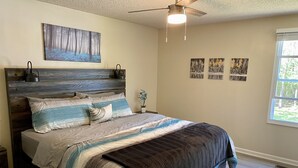 Quarto com cama, ventilador de teto, janela e obras de arte nas paredes.