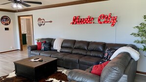Uma sala de estar com sofá seccional, mesa de centro, tapete de couro bovino e um letreiro na parede com a inscrição "Music City".