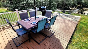 An outdoor deck with a table and chairs, a grill, and a view of a garden. - Streamside Family Friendly Accommodations minutes from Ohiopyle! (Farmington)