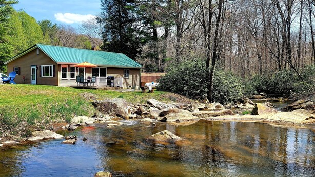 A cabin with a green roof, a porch with outdoor seating, and a small stream in front. - Streamside Family Friendly Accommodations minutes from Ohiopyle! (Farmington)
