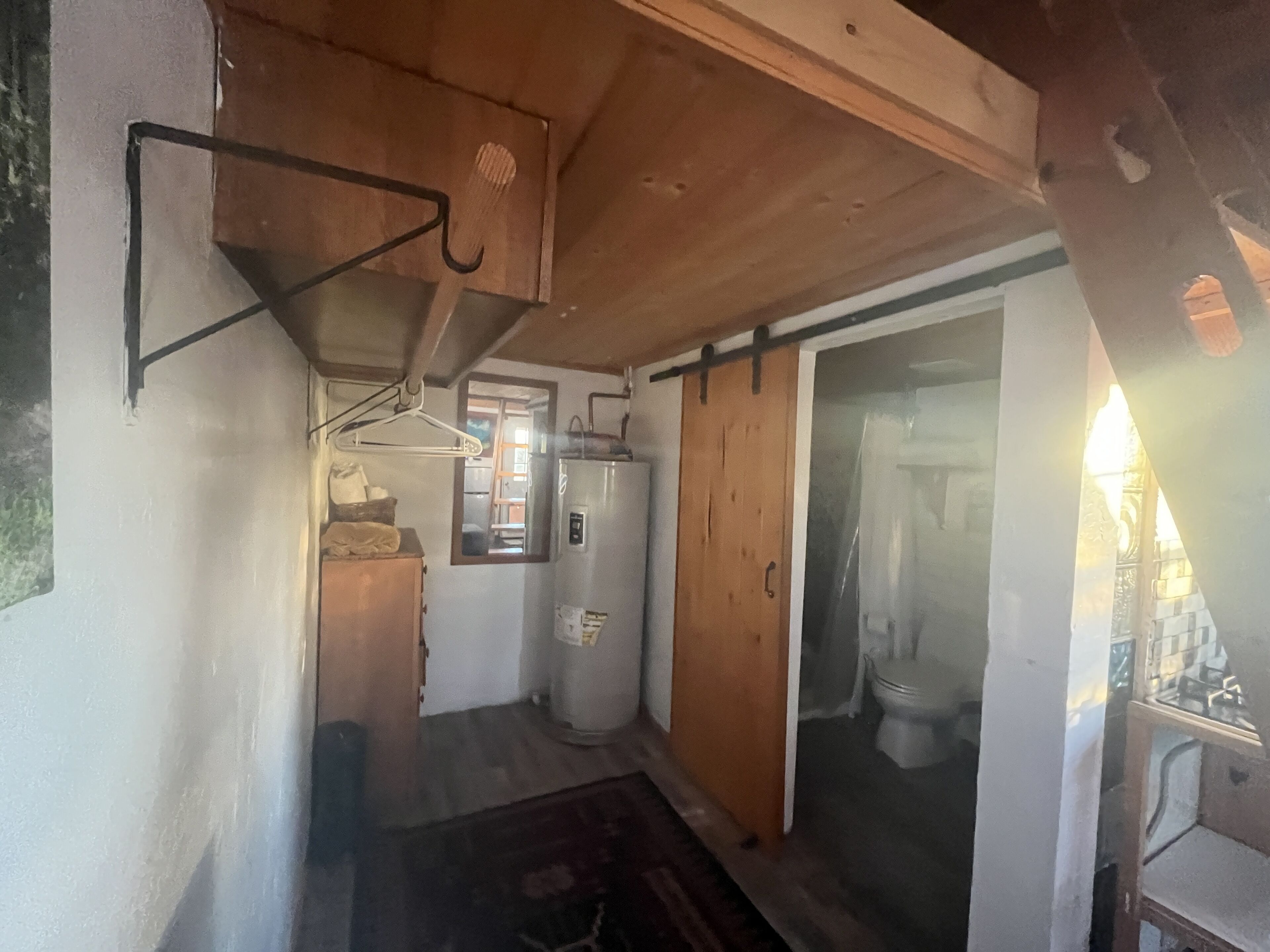 Un pasillo estrecho con techo de madera, un ventanal pequeño y una puerta que da a un baño.
