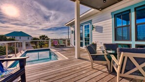 Une terrasse en bois avec une piscine, un espace salon extérieur et une vue sur une maison aux détails et aux fenêtres de couleur turquoise.
