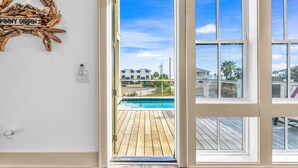 Une pièce dotée d’une grande fenêtre, d’une terrasse en bois et offrant une vue sur une piscine et des bâtiments.